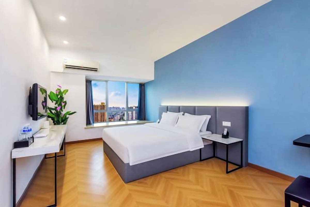 Une chambre d’hôtel moderne avec un grand lit, une table de chevet, une télévision et une fenêtre donnant sur la ville.