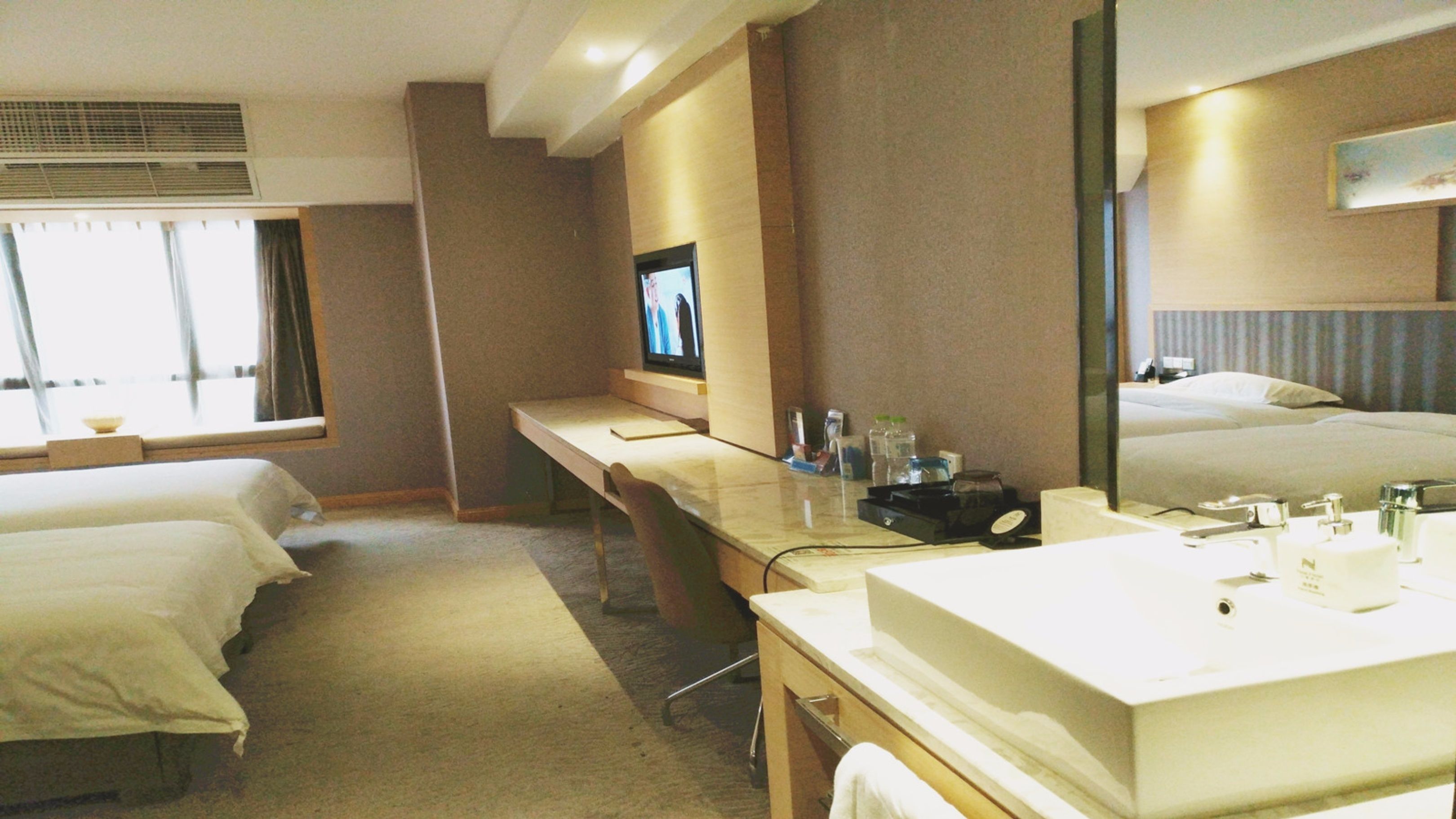 Une chambre d’hôtel avec deux lits, un bureau, un grand miroir et une salle de bain équipée d’un lavabo et d’un miroir.