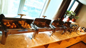Una mesa de buffet con varias estaciones de servicio, una encimera de mármol y una ventana con vistas a edificios.