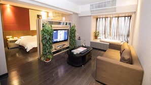 Habitación de hotel con cama, televisión, escritorio con computadora, sofá y ventana con cortinas.