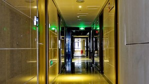 Un pasillo largo y bien iluminado con pisos reflectantes y puertas de vidrio a ambos lados, que conduce a una salida luminosa.
