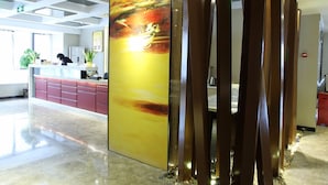 Zona de recepción con diseño moderno, que incluye un cuadro abstracto de gran tamaño, un mostrador de recepción y un panel decorativo de metal.