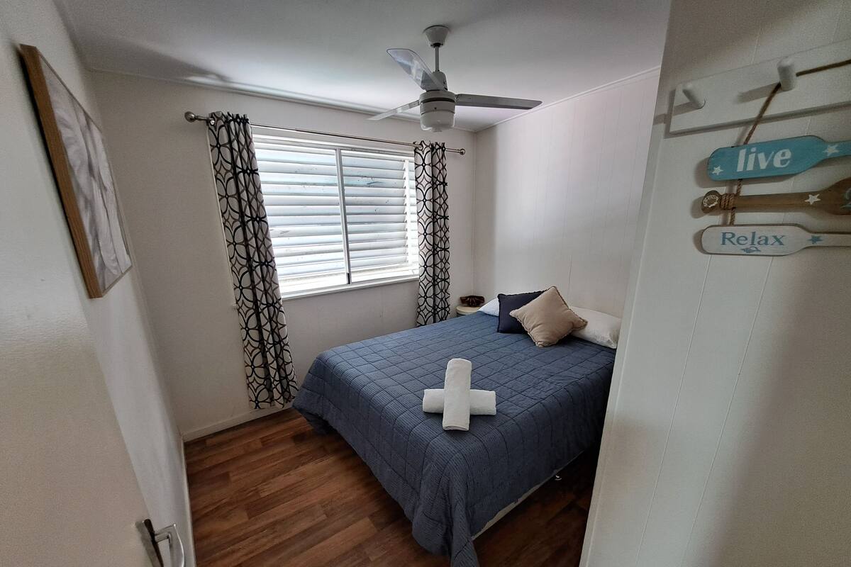 Une chambre à coucher avec un lit, un ventilateur de plafond, une fenêtre avec des rideaux et un panneau mural portant les mots «ivre» et «détendez-vous».
