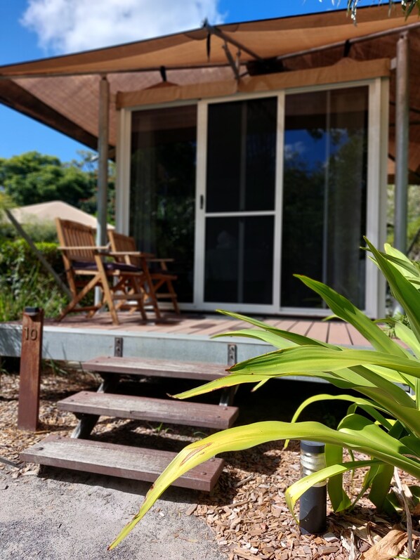 A wooden deck with a chair and a table, leading to a glass door entrance.