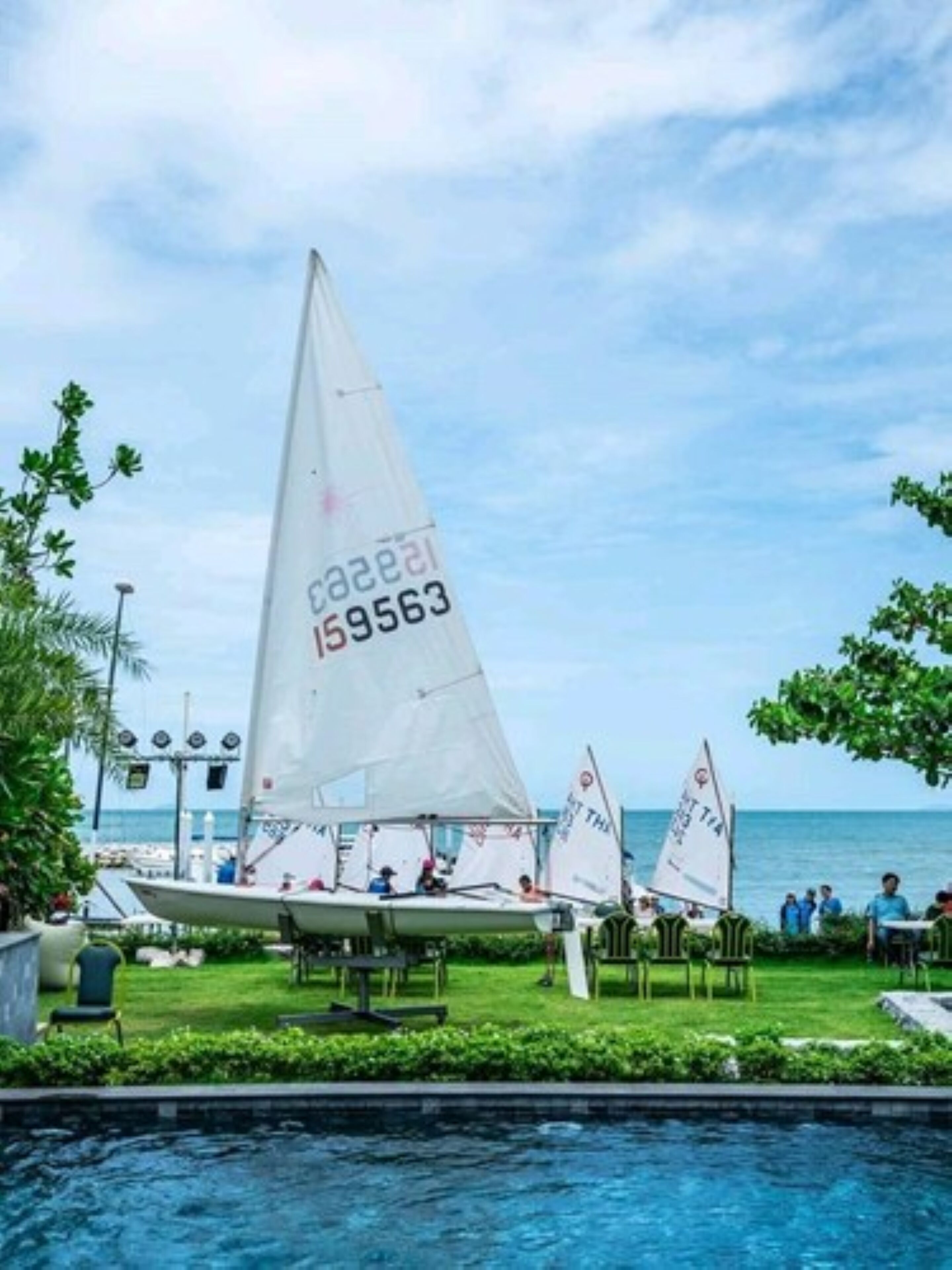 A marina with sailboats docked, a swimming pool, and a view of the sea.