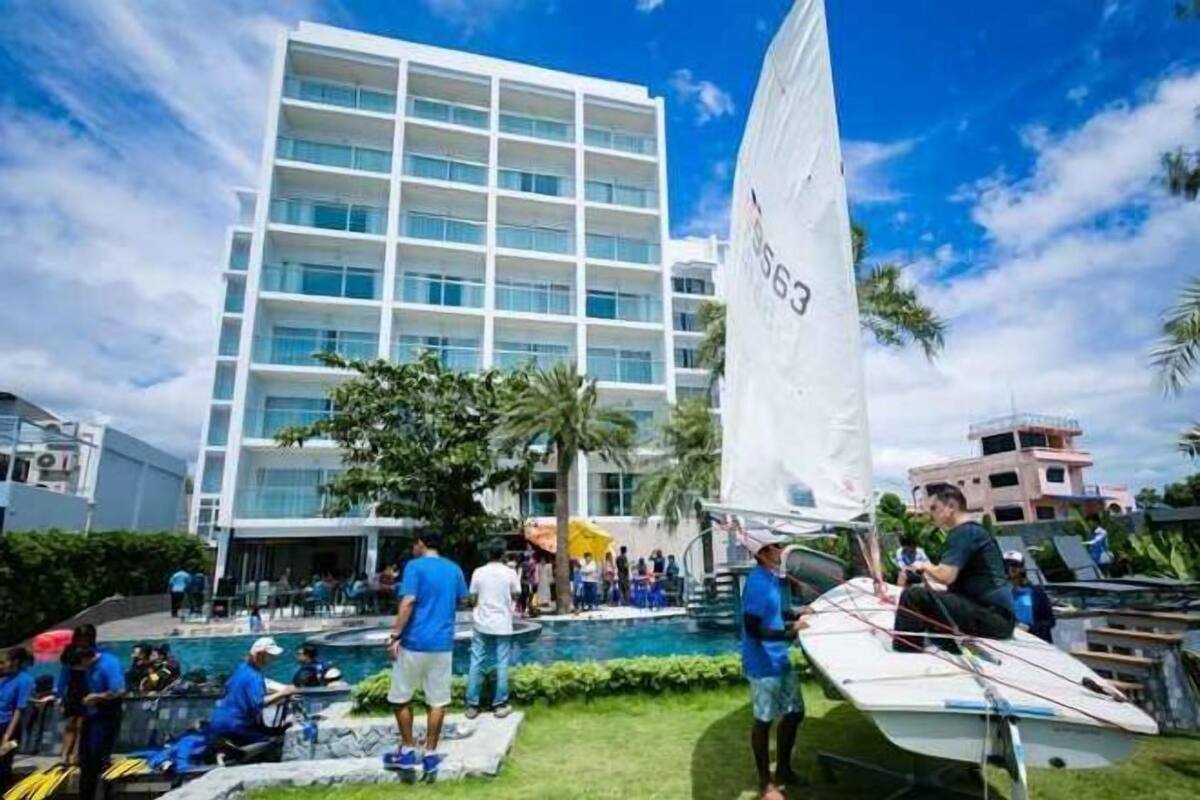 Un hotel moderno con zona de piscina, un velero y gente alrededor.