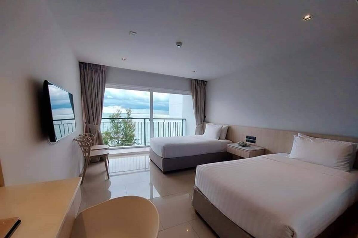 Habitación de hotel con cama, mesita de noche, silla, televisor y balcón con vistas.