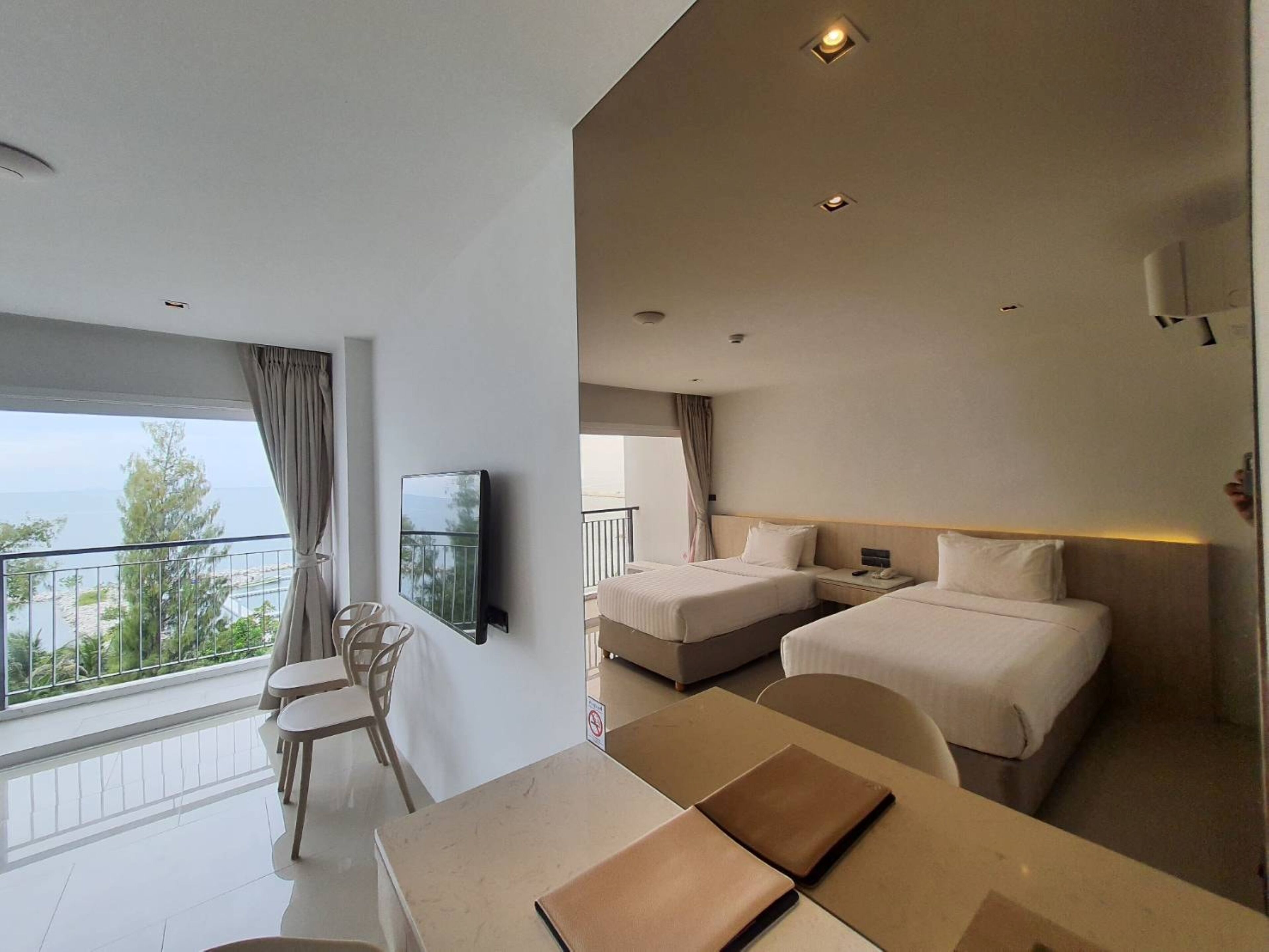 Ett hotellrum med två sängar, ett skrivbord, en stol, en TV och en balkong med utsikt över havet.