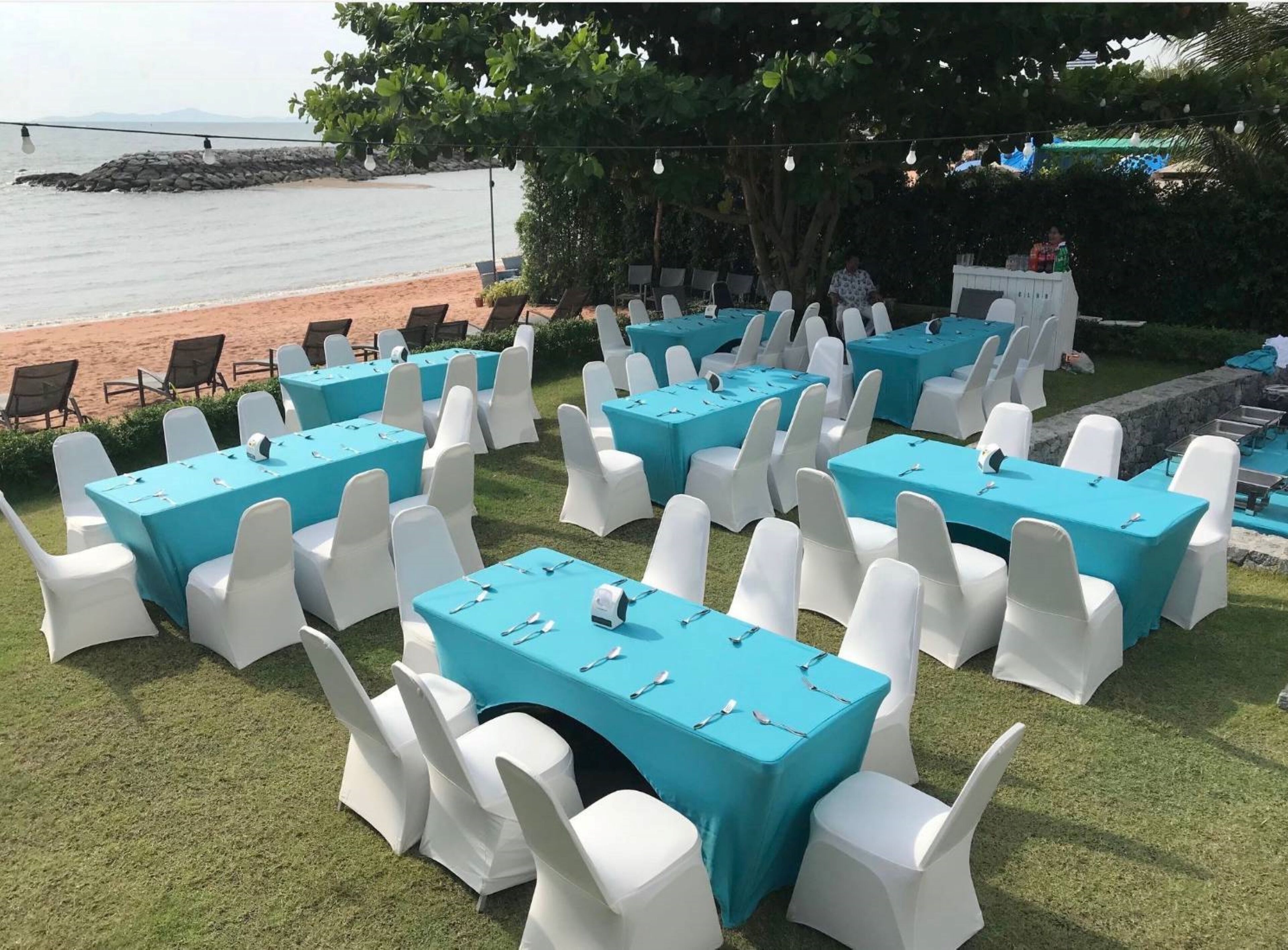 An outdoor event space with multiple tables and chairs, a beach view, and a stone wall.