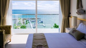 Une chambre d’hôtel avec un grand lit, une vue sur la mer et un balcon donnant sur un port de plaisance.