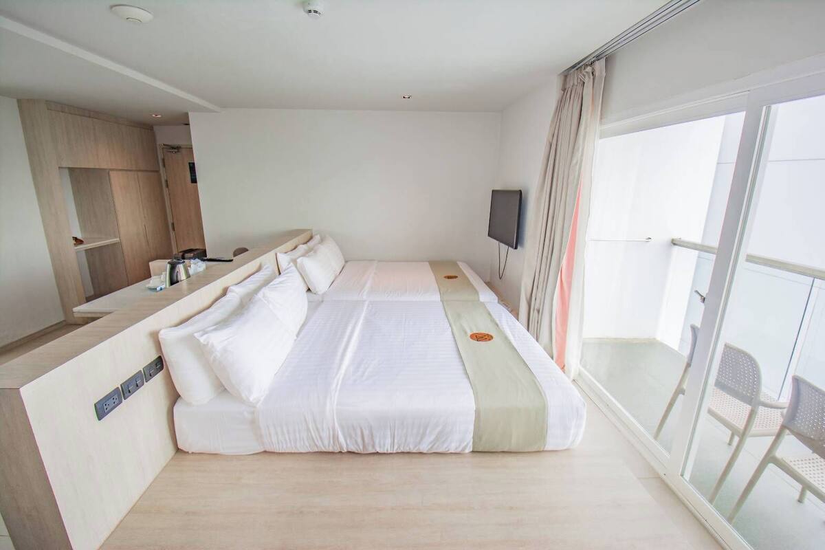 Habitación de hotel moderna con una cama grande, un escritorio, un televisor y un balcón con sillas.