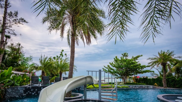 Un espace piscine doté d’un toboggan aquatique, de palmiers et offrant une vue sur l’océan.