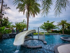Ein Poolbereich mit Wasserrutsche, Palmen und Blick aufs Meer.
