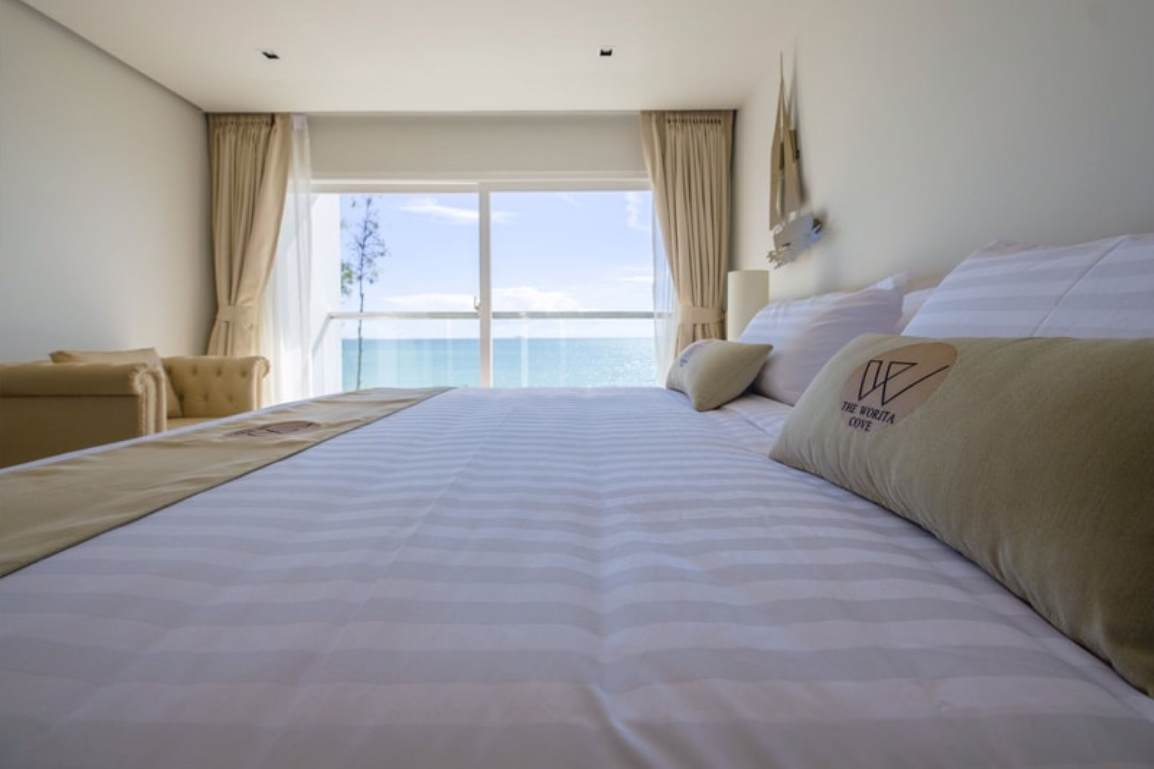 Habitación de hotel con una cama grande, una silla, un ventanal con cortinas y vista al mar.