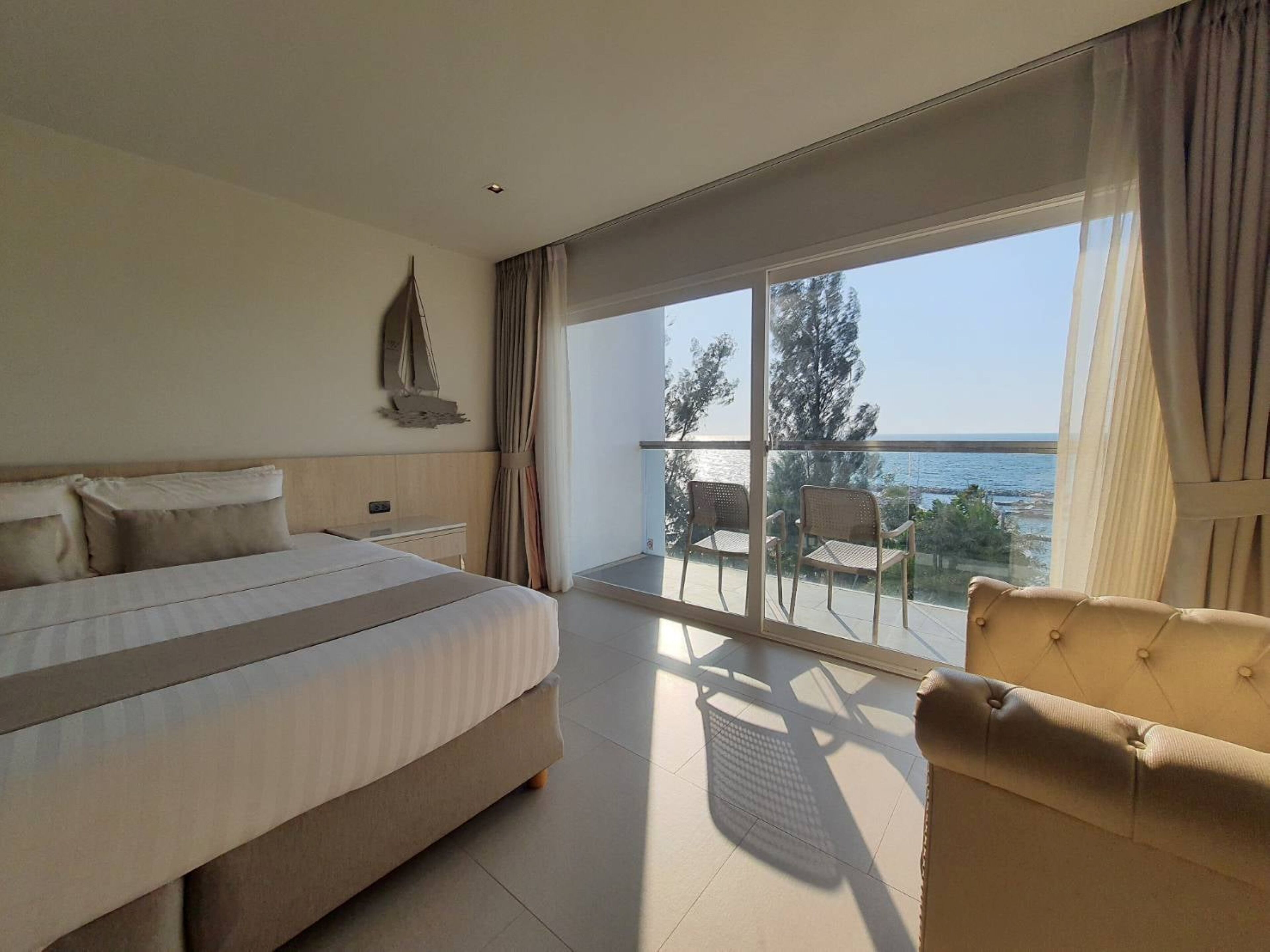 Ein Hotelzimmer mit einem großen Bett, einem kleinen Schreibtisch, einem Sessel und einem Balkon mit Meerblick.