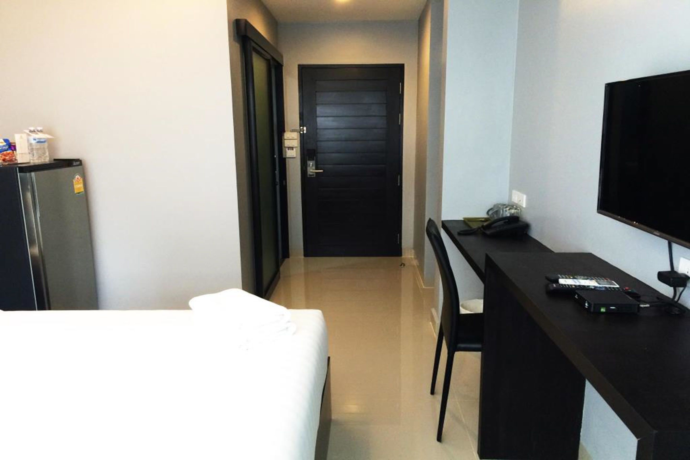 Quarto de hotel com uma cama, uma escrivaninha, uma televisão e uma porta que dá para outro cômodo.