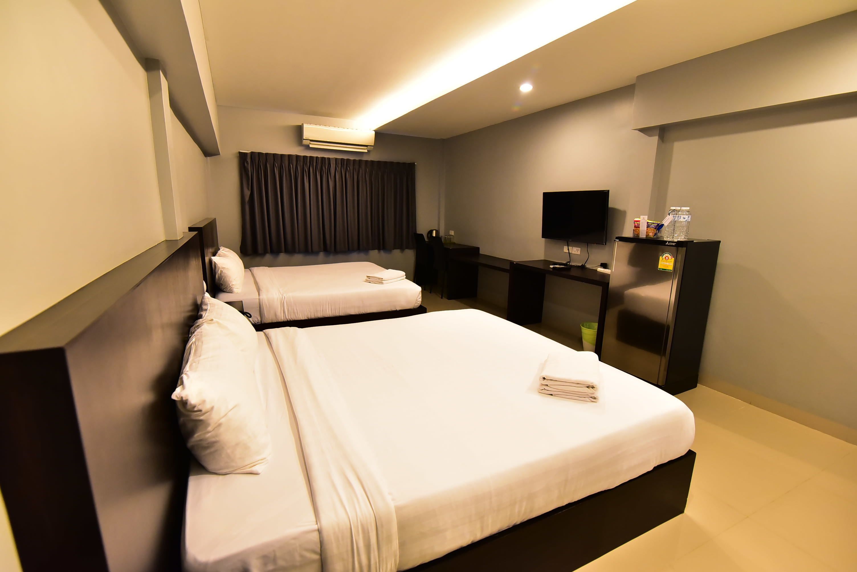 A hotel room with two beds, a desk, a flat-screen TV, and a minibar.
