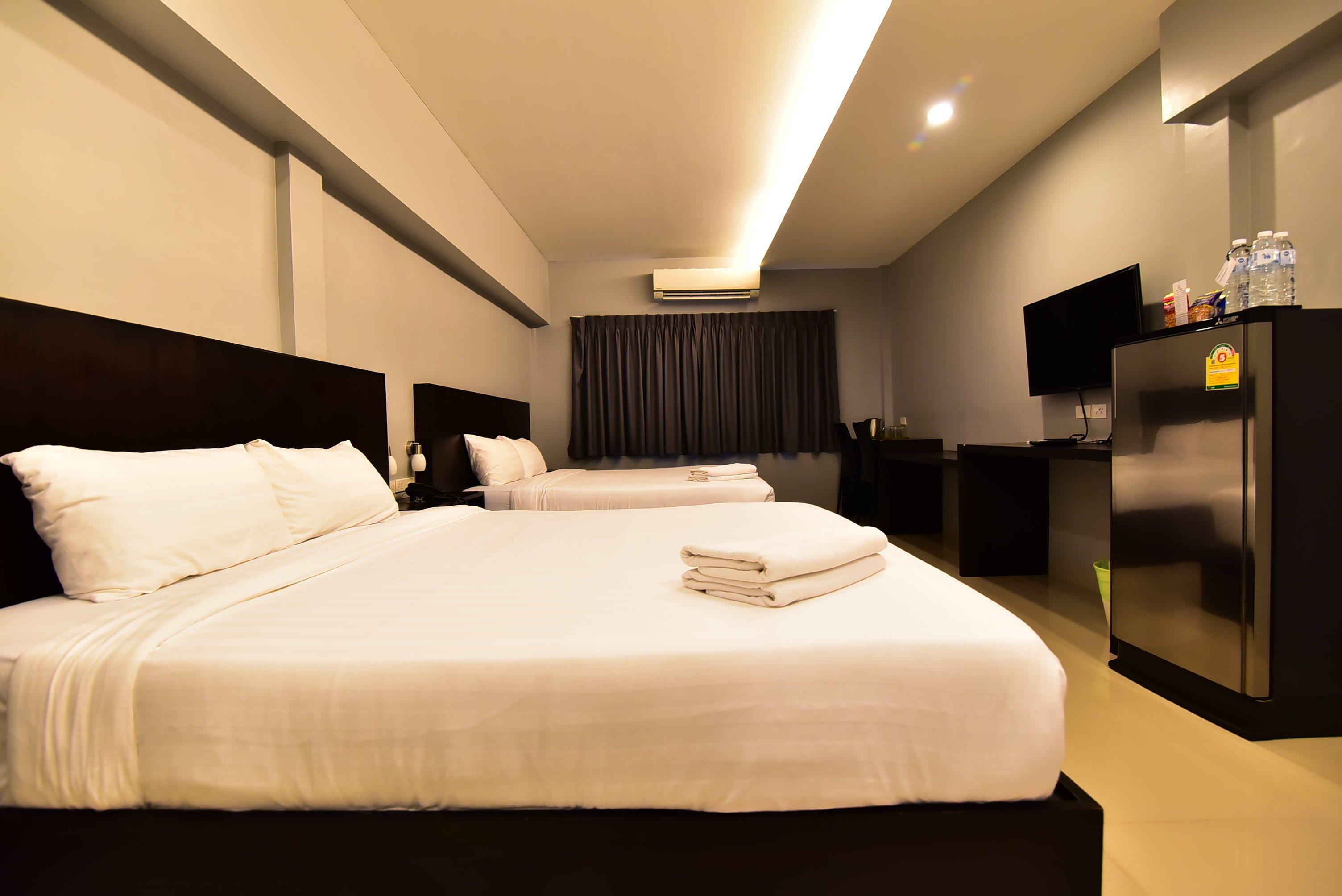 A hotel room with two beds, a flat-screen TV, a refrigerator, and a minibar.