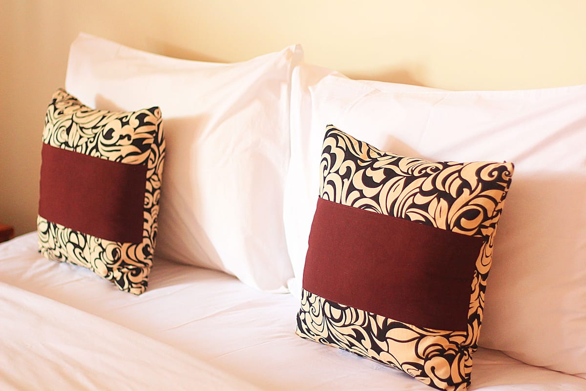 A bed with two decorative pillows featuring a black and beige pattern and a maroon accent.