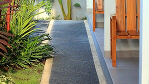 A narrow pathway leading to a wooden bench and a wall with plants. - Sweet Corner Guest House (Denpasar)