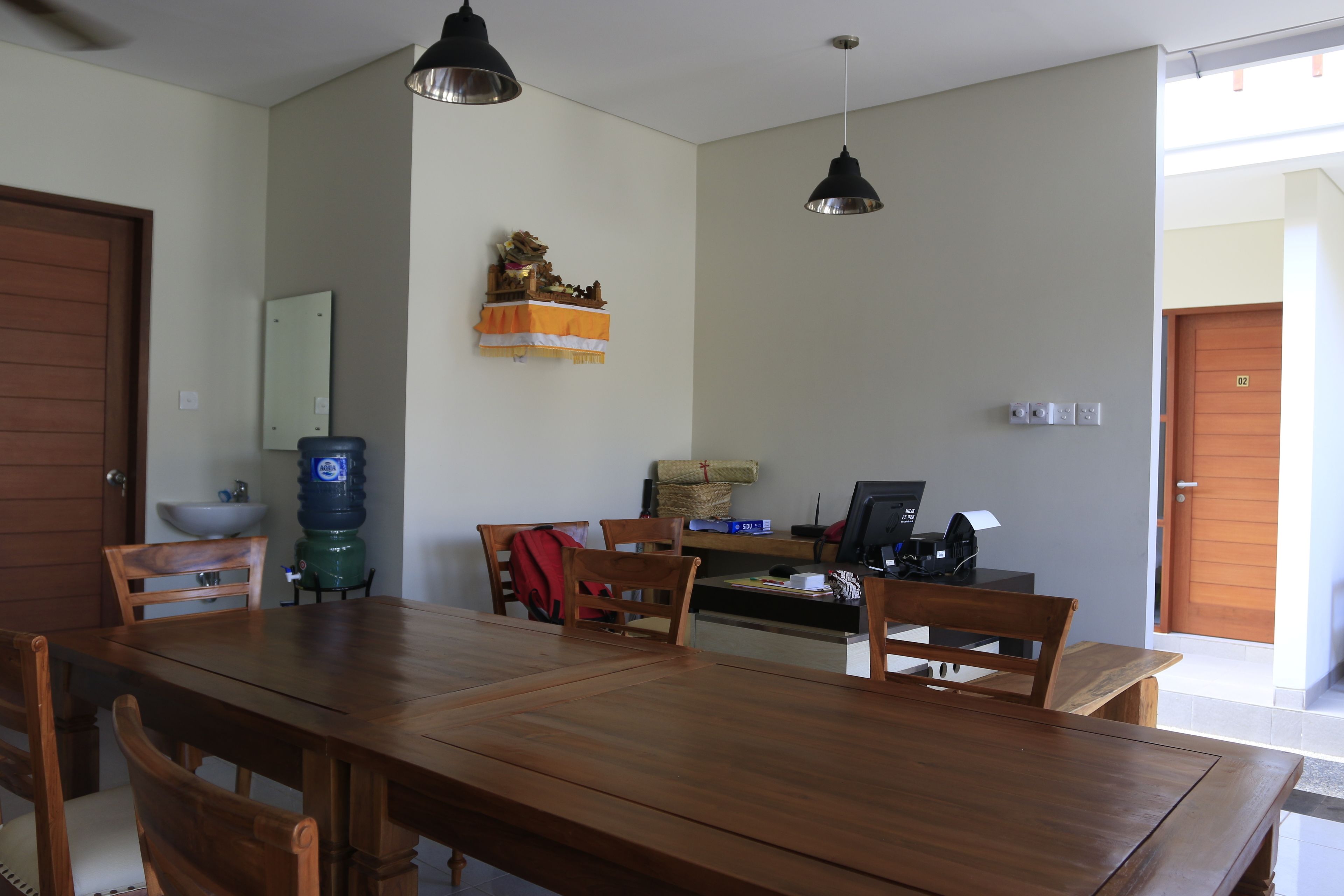 A dining area with a wooden table and chairs, a water dispenser, a computer, and a small shelf with decorative items.
