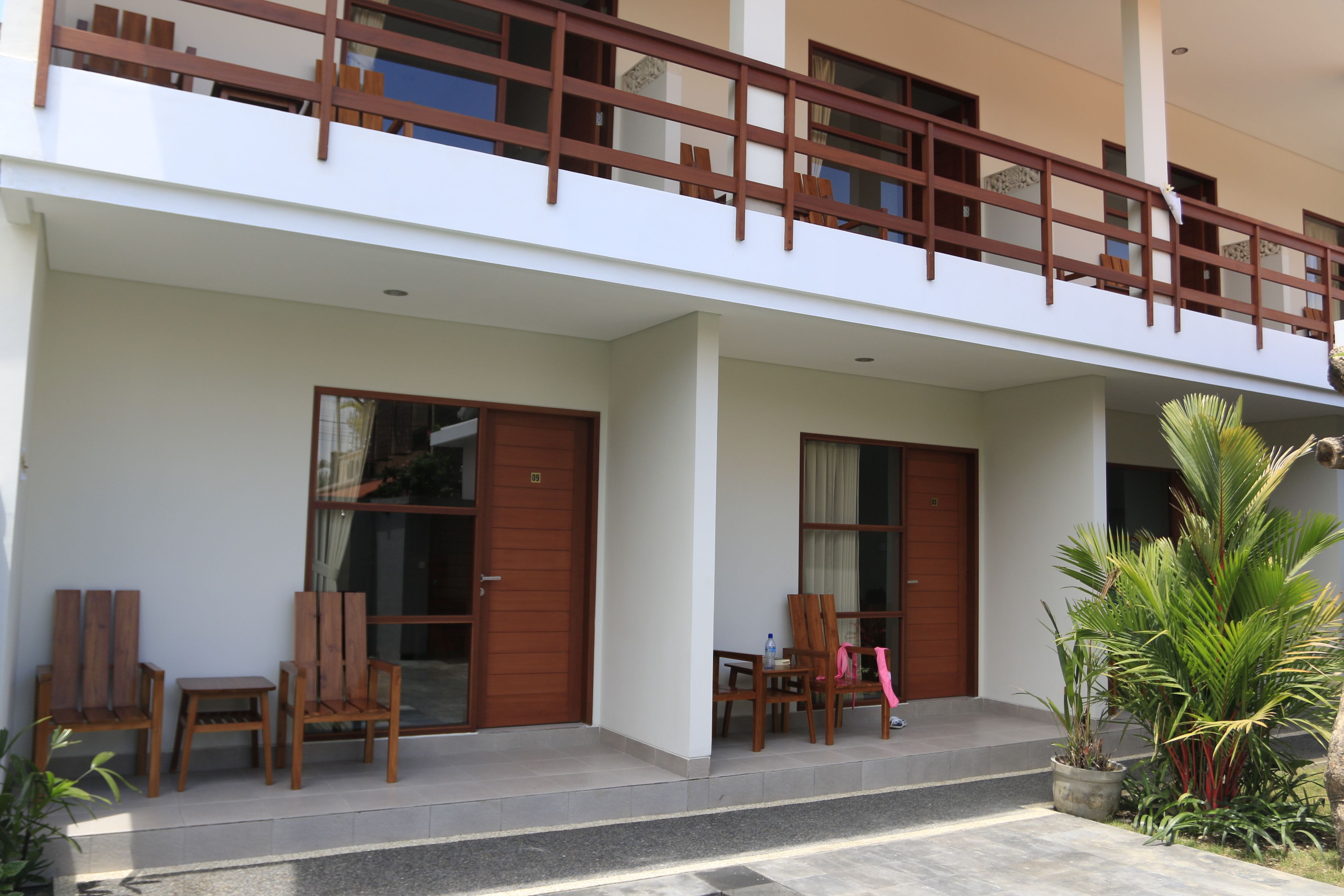 A two-story building with a balcony, wooden doors, and a small outdoor seating area with chairs and a table.