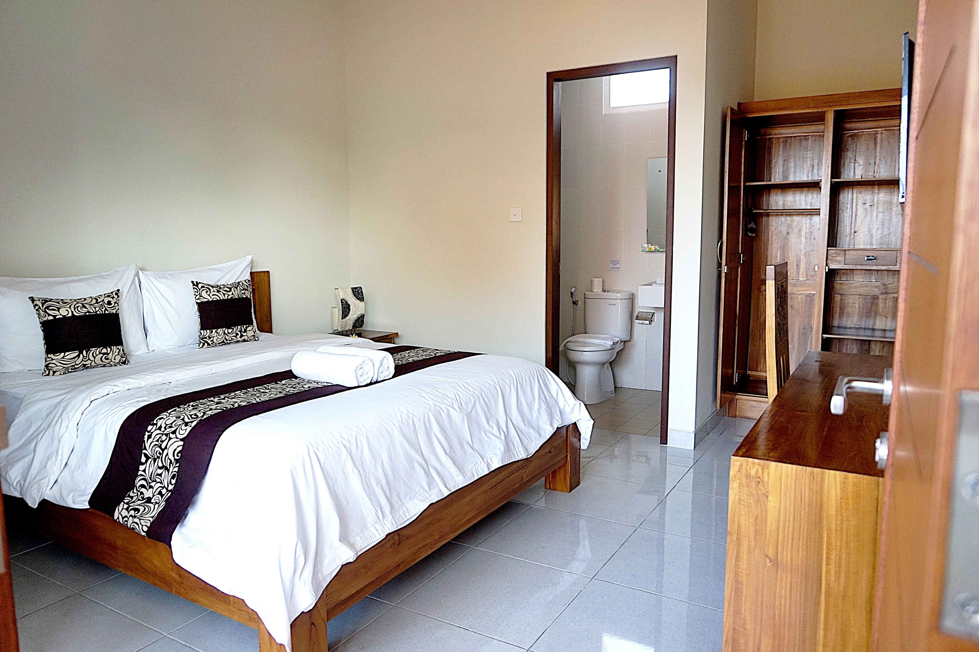 Een slaapkamer met een bed, nachtkastje, kledingkast en een badkamer met toilet en wastafel.