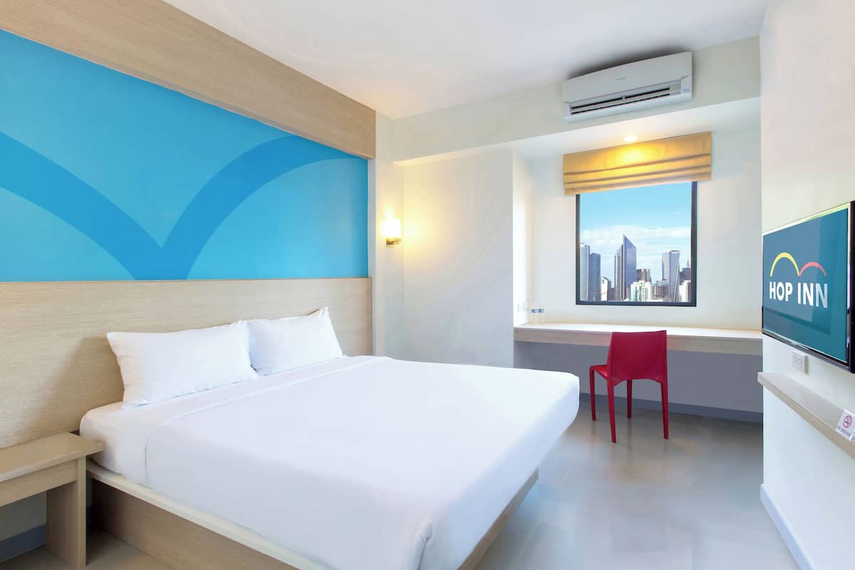A hotel room with a bed, a desk, a chair, a TV, and a window with a city view.