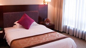 Habitació d'hotel amb un llit gran, una tauleta de nit, una làmpada i una finestra amb cortines.