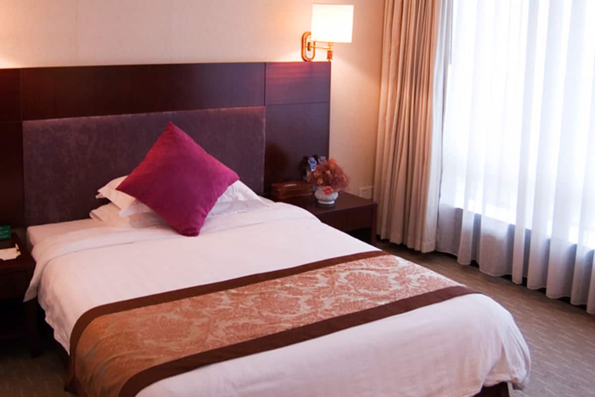 Hotelkamer met een groot bed, nachtkastje, lamp en raam met gordijnen.