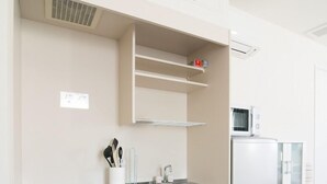 A modern kitchen with white cabinetry, a stainless steel refrigerator, a microwave, and a sink. - Etavia Yufuin ekimae (Yufu)