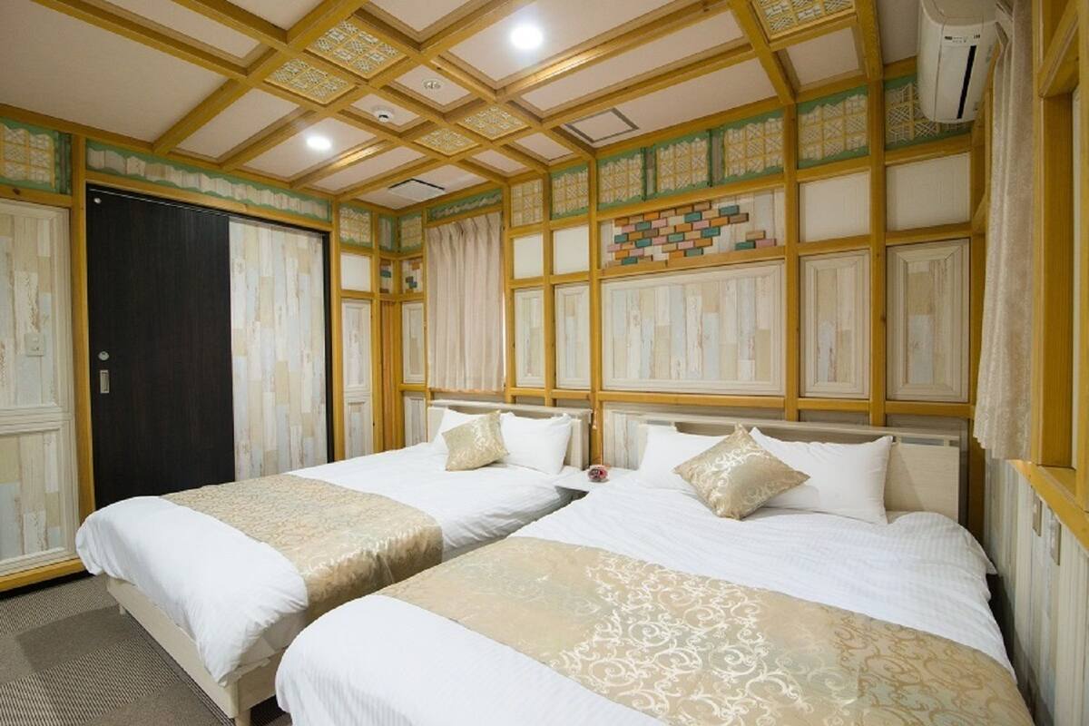 A hotel room with two beds, a dark door, and a decorative ceiling.