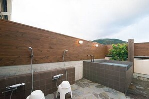 A modern outdoor bathroom with a wooden wall, two showerheads, and a stone-tiled floor. - Etavia Yufuin ekimae (Yufu)