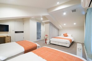 A hotel room with two beds, a desk, a television, and a ceiling fan. - Etavia Yufuin ekimae (Yufu)