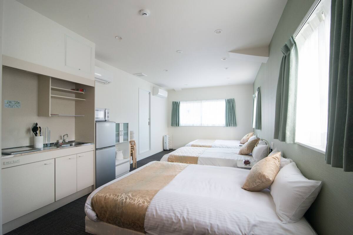 A hotel room with two beds, a kitchenette, and a large window with curtains.