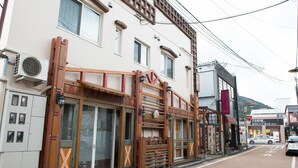 A building with a traditional architectural style, featuring wooden beams and a large window. - Etavia Yufuin ekimae (Yufu)