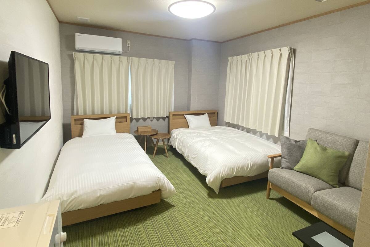 A hotel room with two single beds, a sofa, a small table, and a TV mounted on the wall.