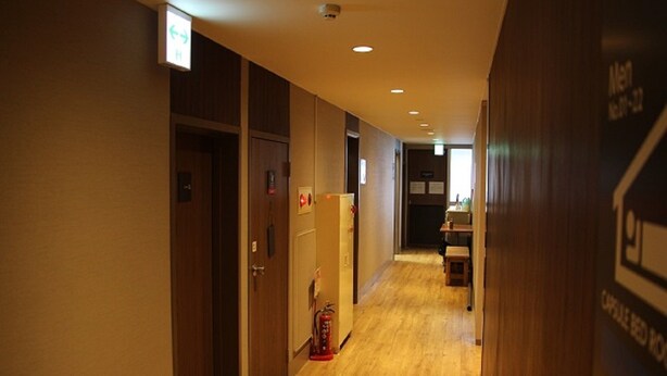 Un couloir d’hôtel avec un plancher, des portes et un extincteur en bois.