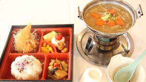 Une boîte à bento contenant du riz, des légumes et un morceau de poulet frit, ainsi qu’un pot de soupe aux carottes et à d’autres légumes.