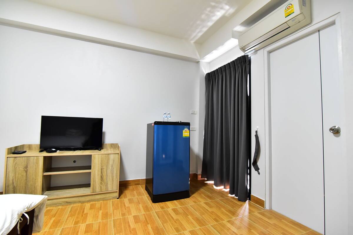 A hotel room with a wooden entertainment unit, a blue refrigerator, a white wardrobe, and a curtain.