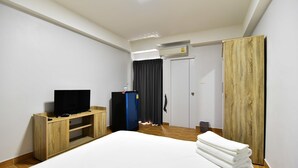 A hotel room with a bed, a TV on a wooden stand, a blue refrigerator, a wardrobe, and a door with a curtain. - WJ Residence at Suvarnabhumi (Bang Phli)