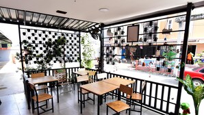 An outdoor cafe with wooden tables and chairs, a metal fence, and potted plants. - WJ Residence at Suvarnabhumi (Bang Phli)