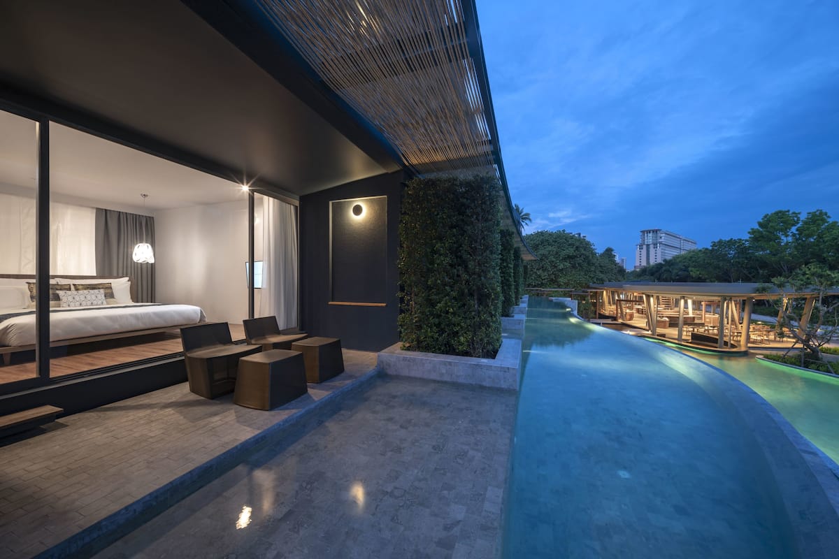 A modern hotel room with a large bed, seating area, and a pool.