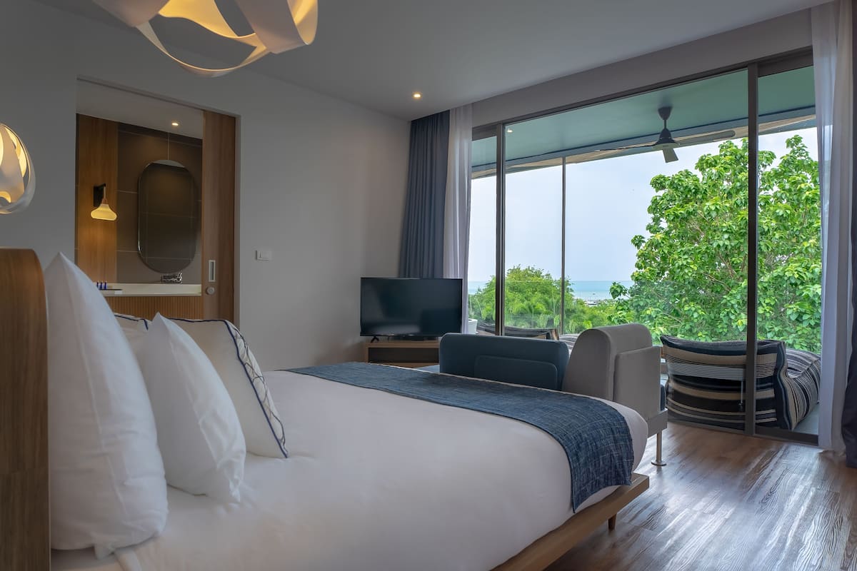 A modern hotel room with a large bed, a TV, and a view of the outdoors.