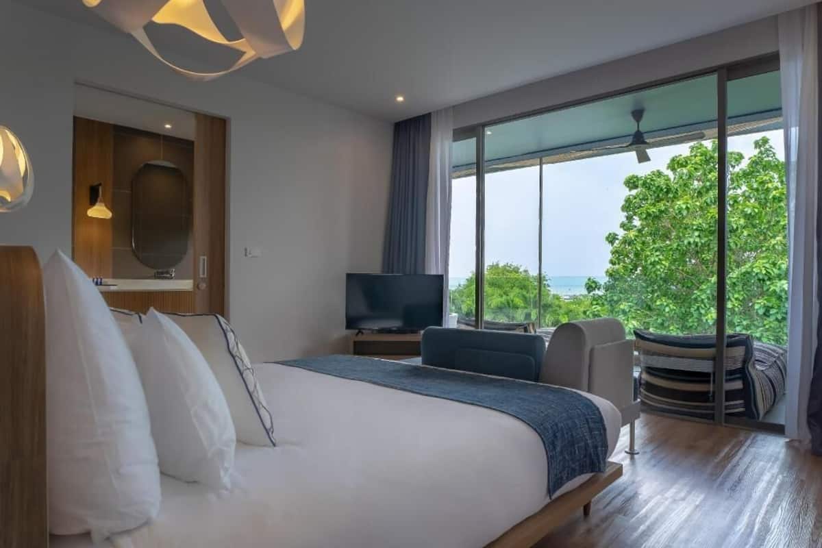 A modern hotel room with a large bed, a television, a seating area with a view of the outdoors, and a balcony with a view of the sea.
