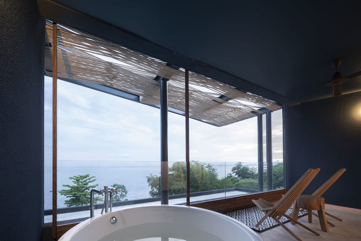 A modern bathroom with a large bathtub, a view of the sea, and a wooden chair.
