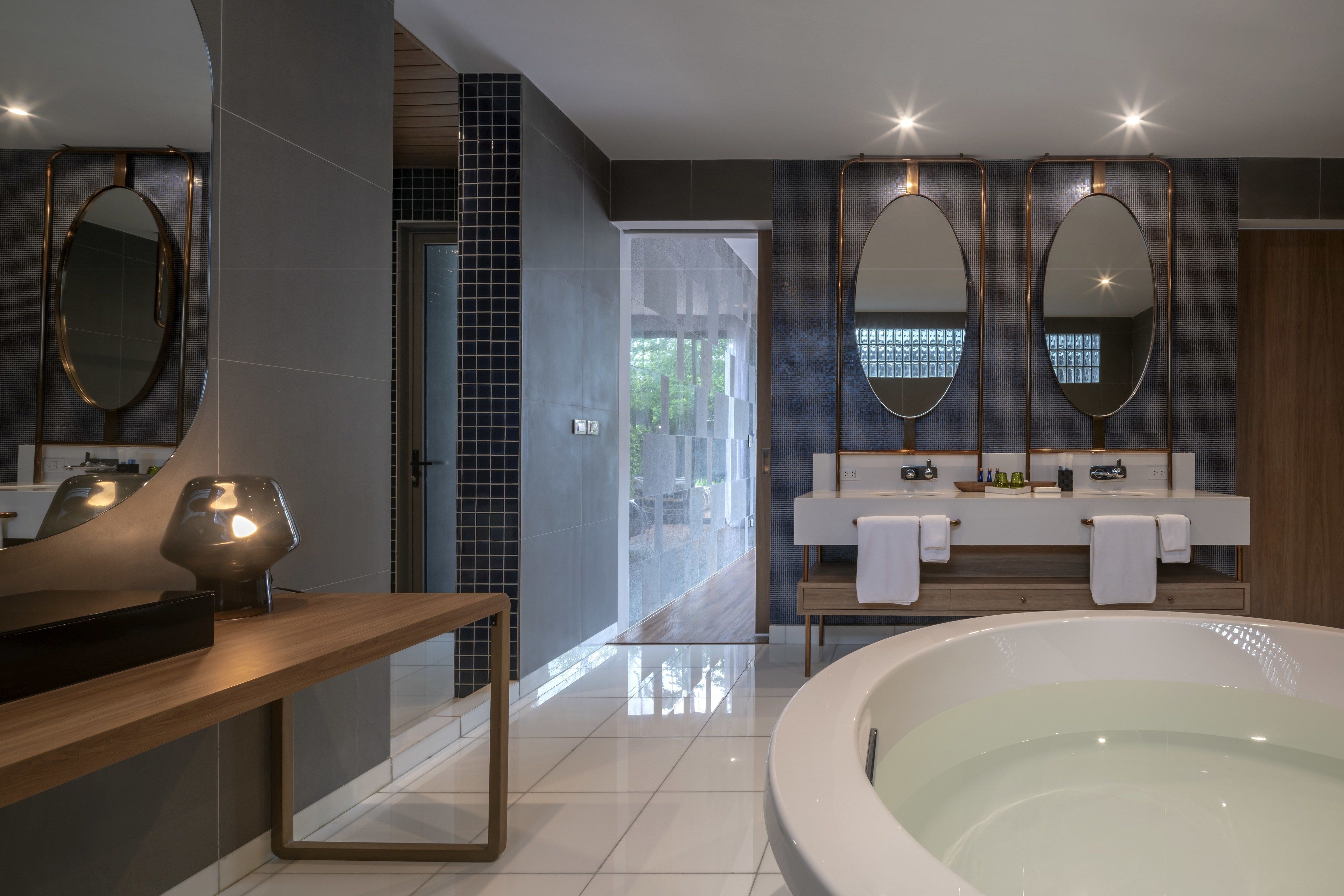 A modern bathroom with a large bathtub, double sinks with mirrors, and a vanity with toiletries.