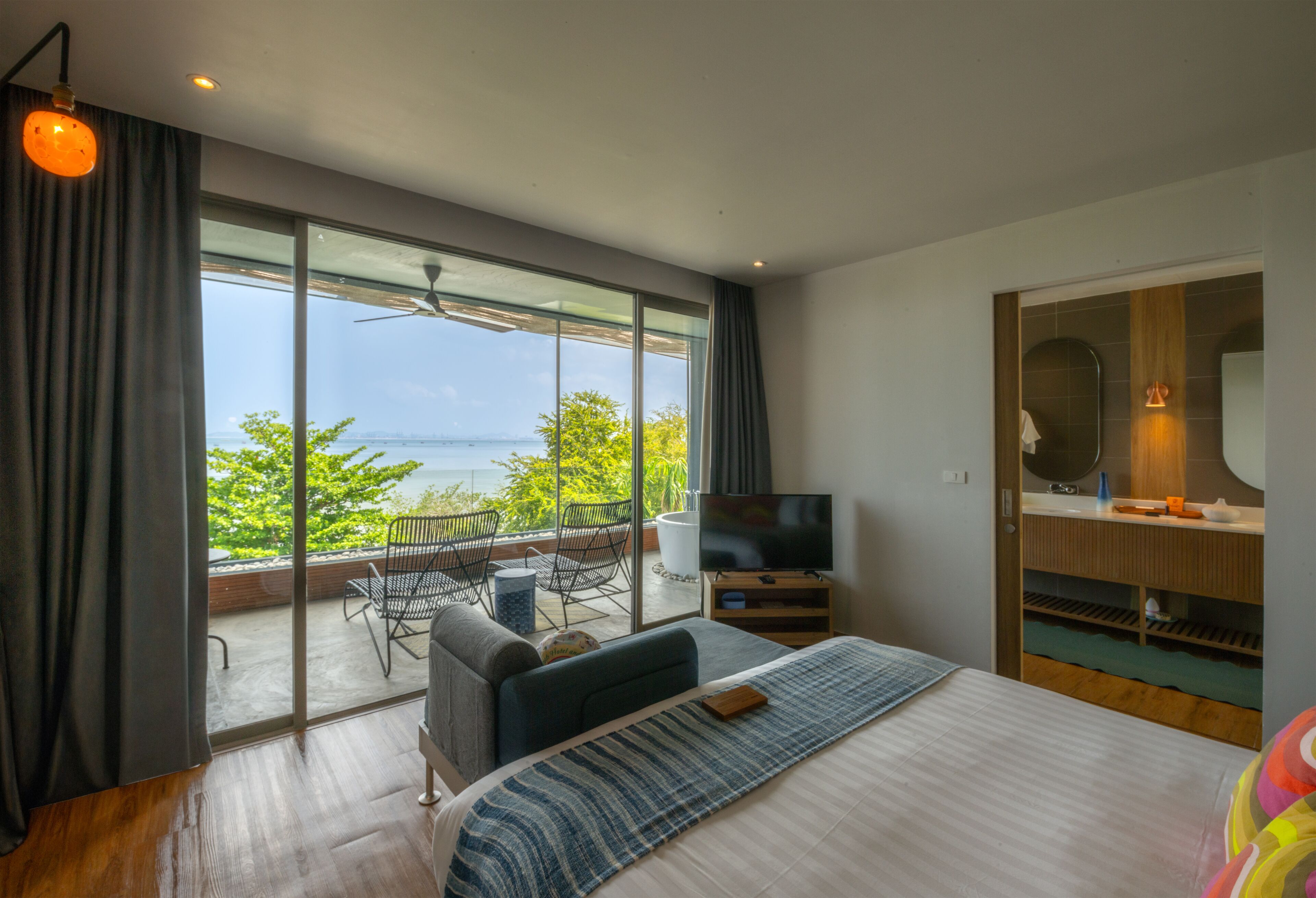 Ein Schlafzimmer mit großem Fenster, einem Bett, einem Fernseher, einem Sessel und einem kleinen Balkon.