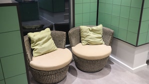 Two wicker chairs with cushions, positioned in a corner with a green tiled wall behind them. - L42 Hostel (Bangkok)