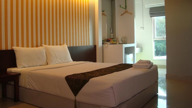 A hotel room with a large bed, a bedside table, a mirror, a wardrobe, and a window with a view of greenery. - L42 Hostel (Bangkok)